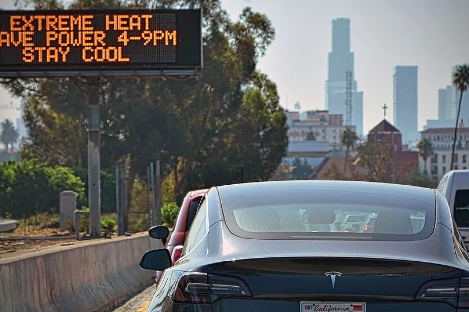 Cars in traffic jam on Los Angeles highway with road sign in center median warning of extreme heat.